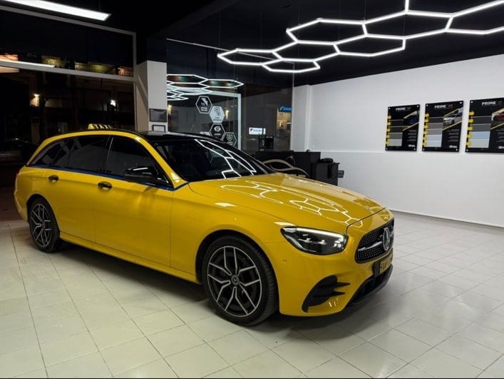 Yellow Mercedes-Benz E-Class estate Athens taxi with its TAXI roof sign, photographed side-on in a detailing studio