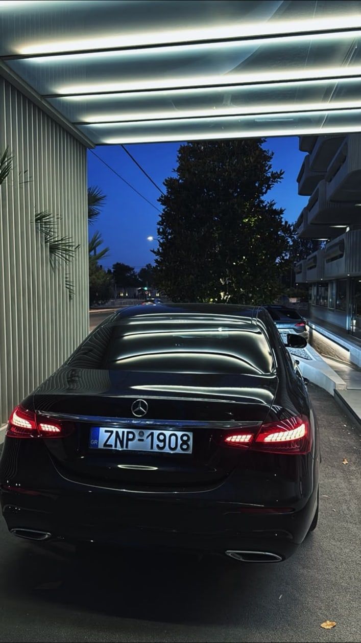 Black Mercedes-Benz E-Class sedan of the MX Transfers fleet waiting under a lit canopy in Athens