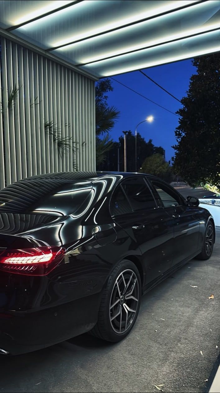 Black Mercedes-Benz E-Class sedan of the MX Transfers fleet parked under a lit canopy at night in Athens